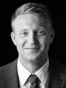 Zwart-wit portret van Felix in pak met stropdas tegen een donkere achtergrond.